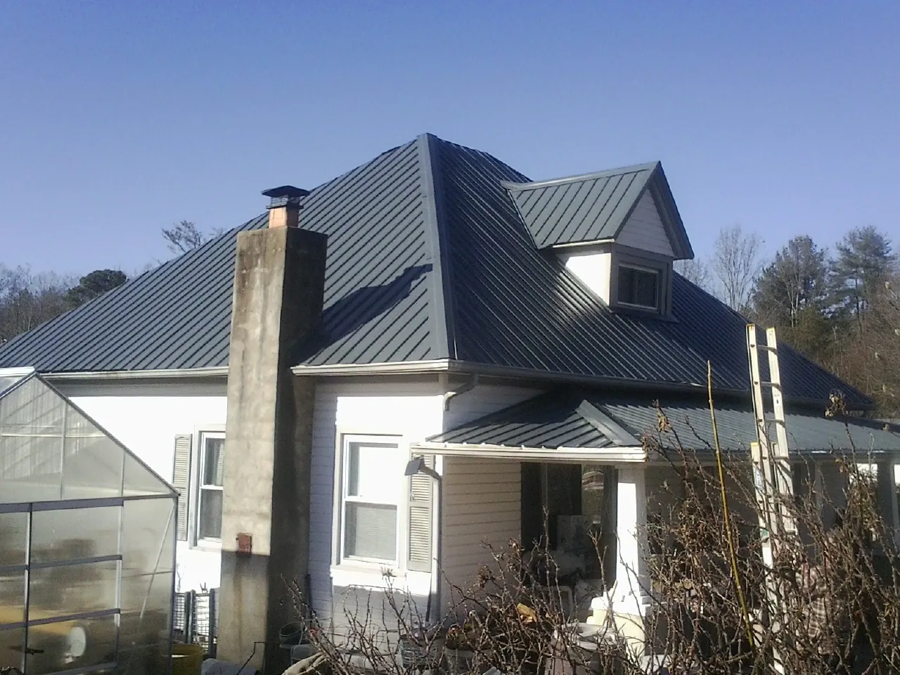 Dark blue standing seam metal roof on a white farmhouse with dormer — Slate & Tile Roof Repair by Roofing Brothers in Wildersville
