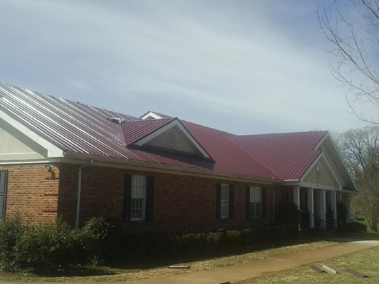 Red metal roof with gabled entries on a long brick building, from a Hail Damage Roof Repair job in Wildersville