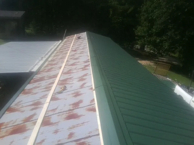 Old rusted panels beside newly installed green metal roofing — Wind Damage Roof Repair by Roofing Brothers in Wildersville