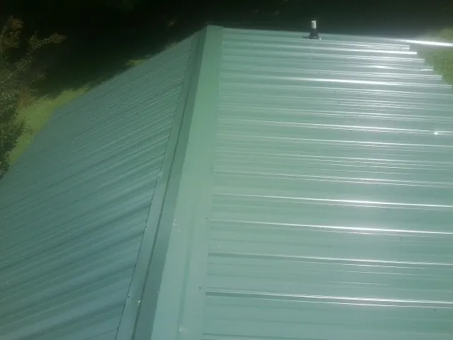 New green metal panels meeting at the ridge of a roof — Flat Roof Repair work by our crew in Wildersville