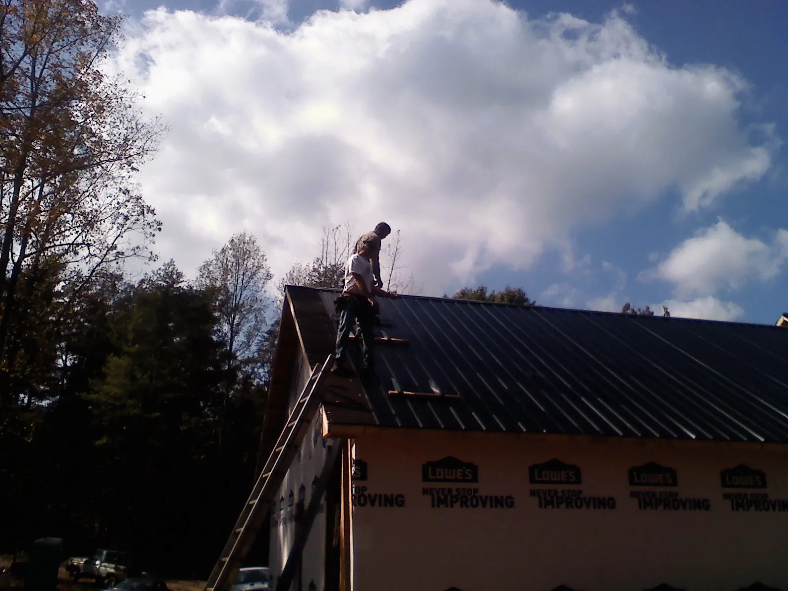 Roofer fastening dark metal panels high against a cloudy sky, from a Roof Inspection job in Wildersville
