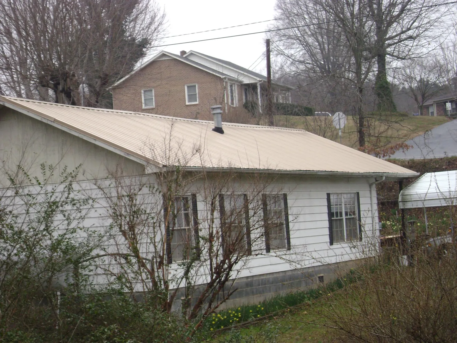 Tan metal roof on a white sided house set into a hillside — Commercial Roofing by Roofing Brothers in Wildersville